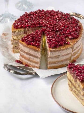 whole pomegranate mousse cake sliced with slice out on a plate in the foreground