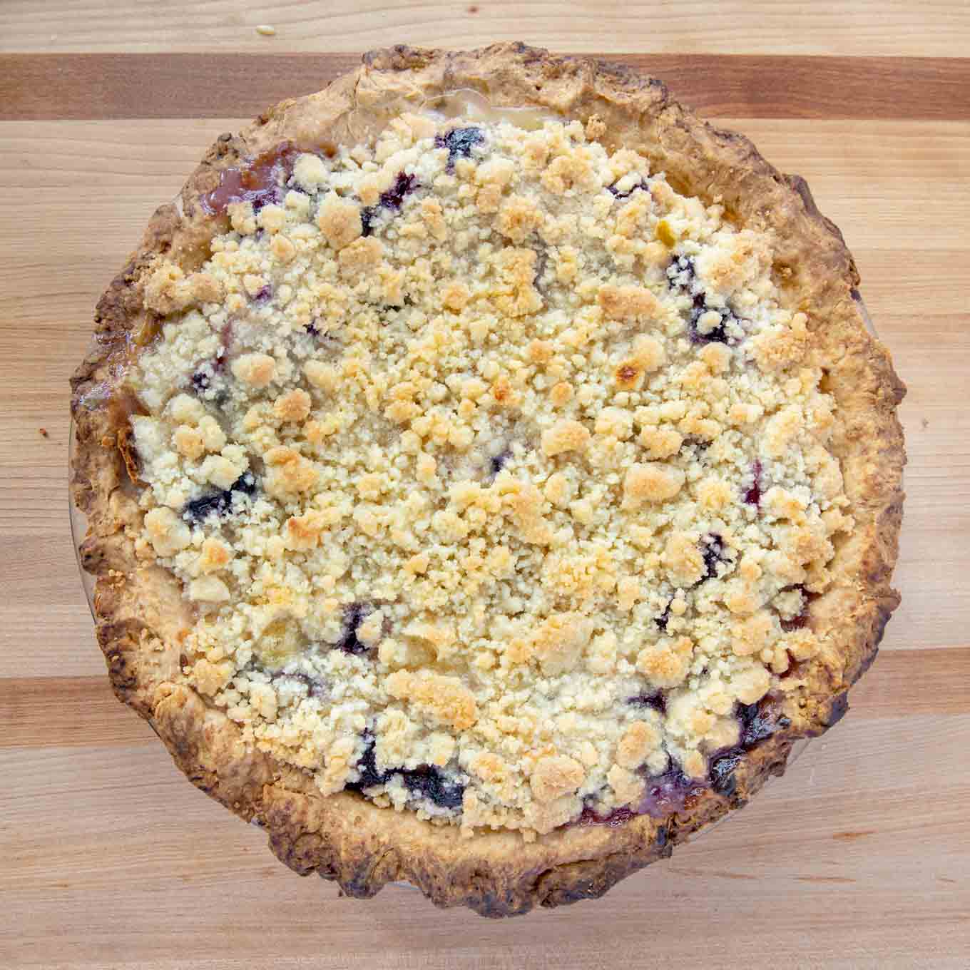 fully baked peach blueberry custard pie on a wooden cutting board