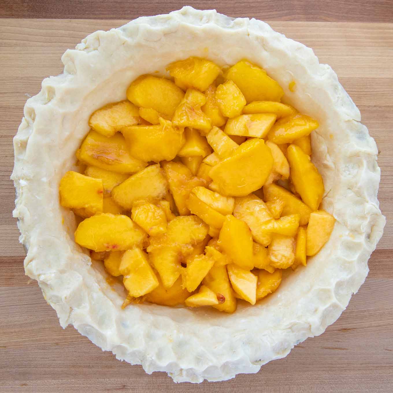 Pie crust in a glass pie pan with a layer of sliced peaches in the pie shell