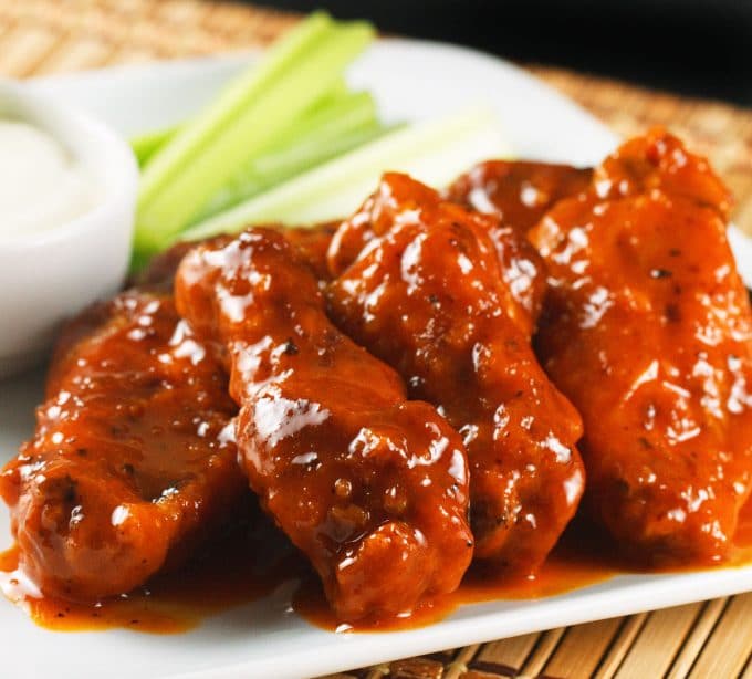 buffalo wings with bleu cheese dressing and celery sticks blurred in the background on a white plate