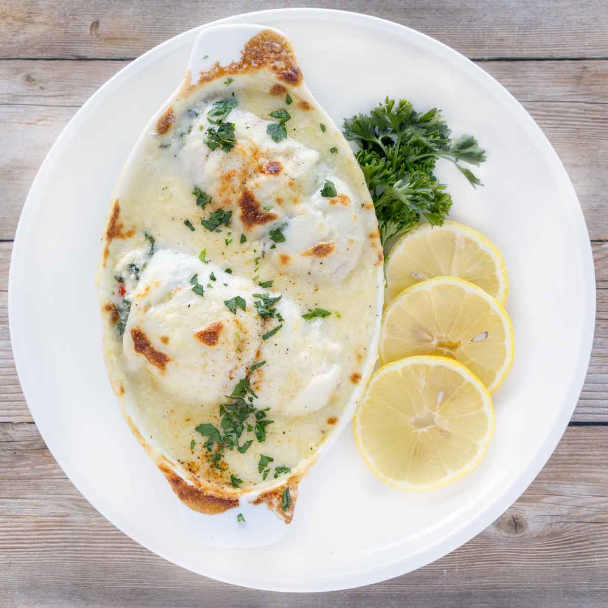 baked stuffed flounder in a white casserole dish on a white plate with lemons and parsley
