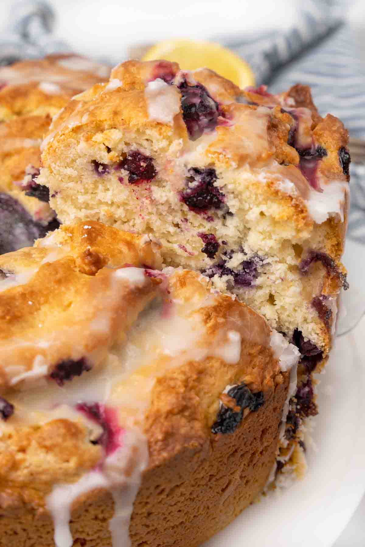 Slice of lemon blueberry cake being taken out of whole cake.