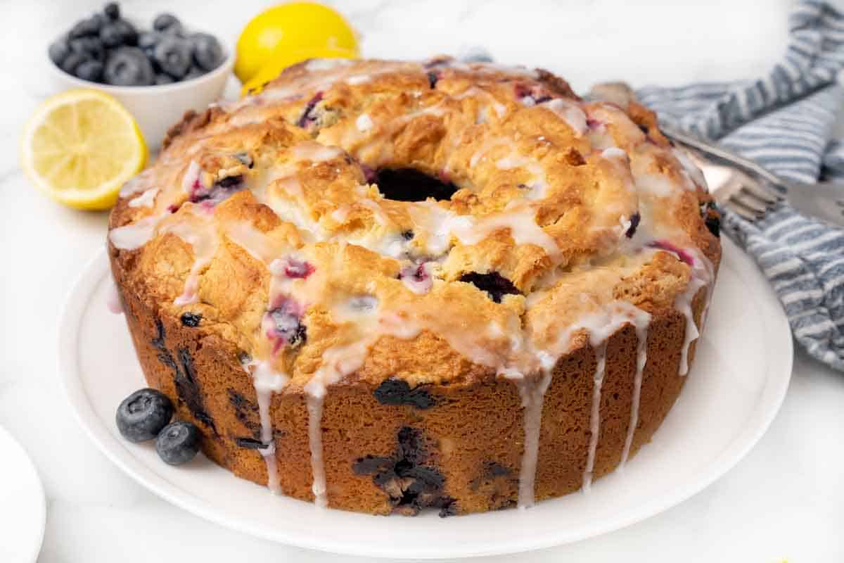Whole lemon blueberry pound cake with glaze on a white platter.