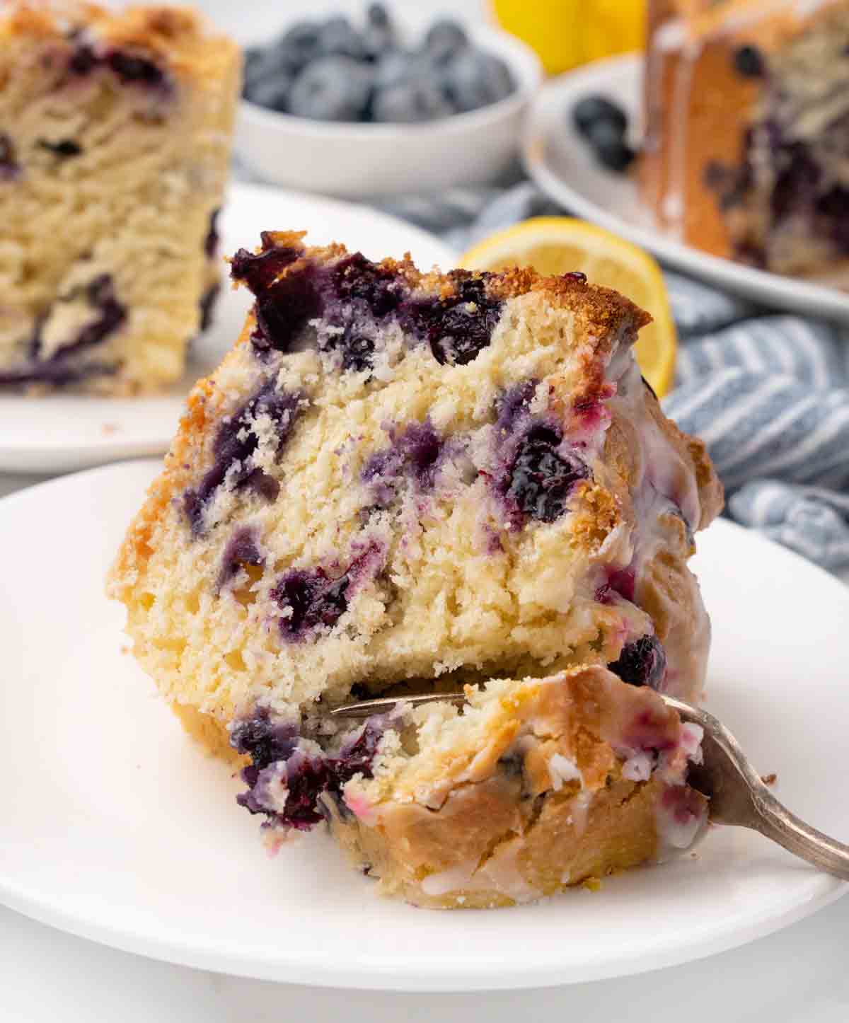 Slice of lemon blueberry pound cake with a fork in it on a white plate.