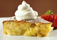 pineapple butter cake with whipped cream sitting on a white plate with strawberry on a brown background