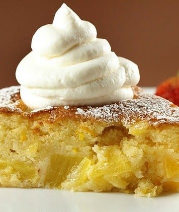 pineapple butter cake with whipped cream sitting on a white plate with strawberry on a brown background