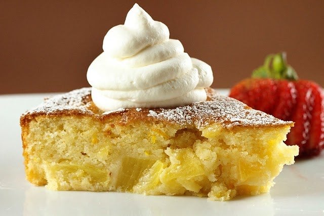 pineapple butter cake with whipped cream sitting on a white plate with strawberry on a brown background