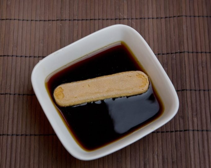ladyfinger soaking in a container of coffee and coffee liqueur 
