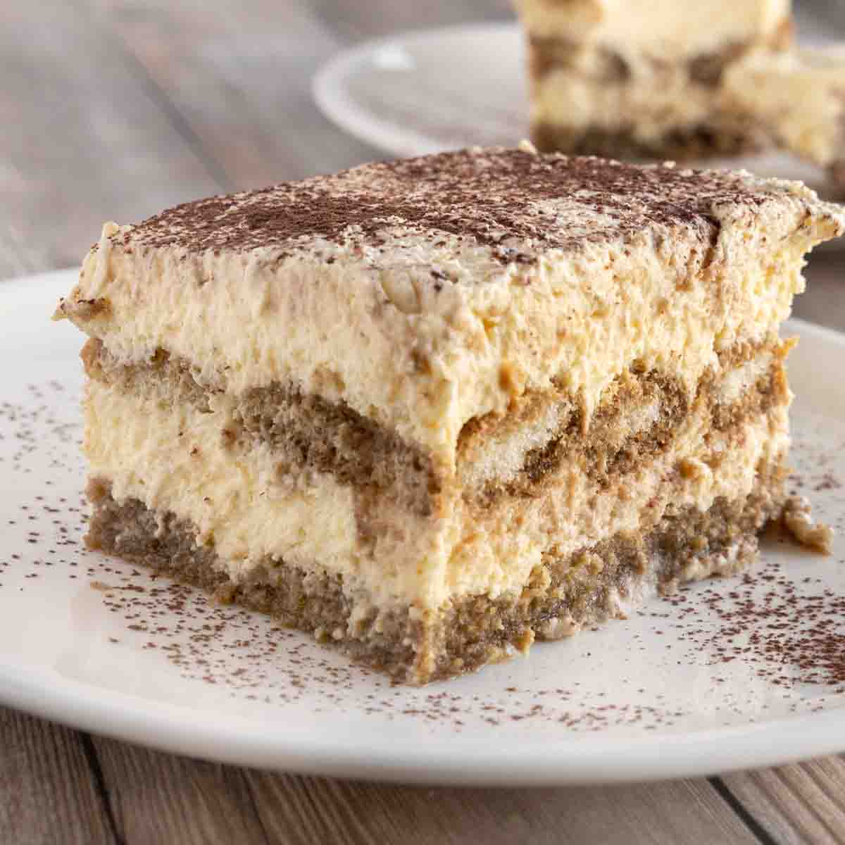 Slice of tiramisu on a white plate, dusted with cocoa powder.