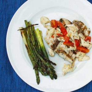 grilled mahi-mahi topped with crabmeat and grape tomatoes on a white plate with grilled asparagus