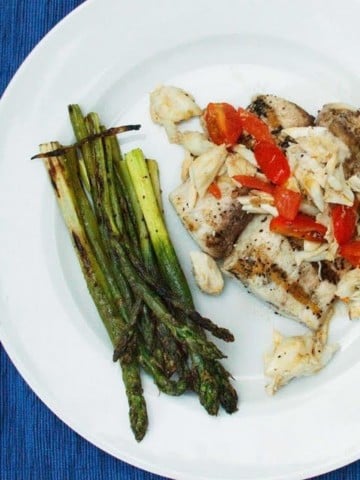 grilled mahi-mahi topped with crabmeat and grape tomatoes on a white plate with grilled asparagus