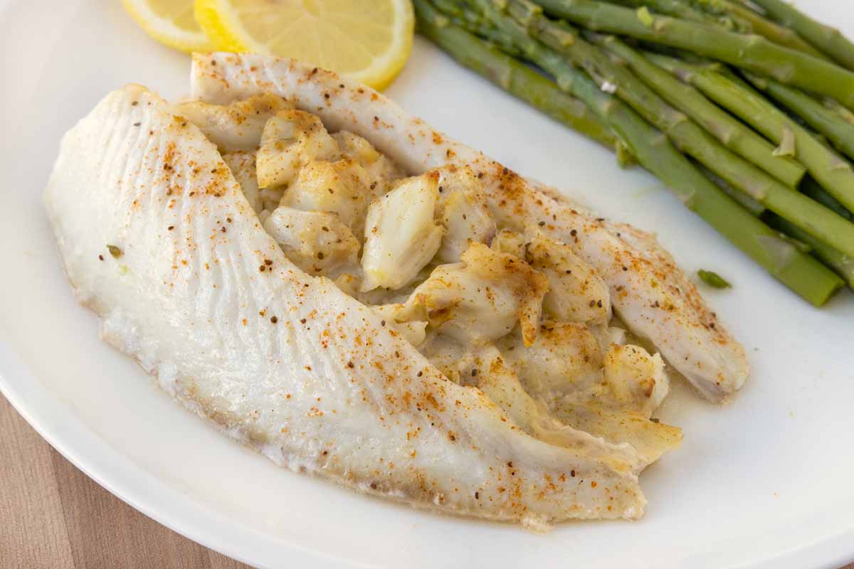 Stuffed flounder on a white plate with asparagus and lemons