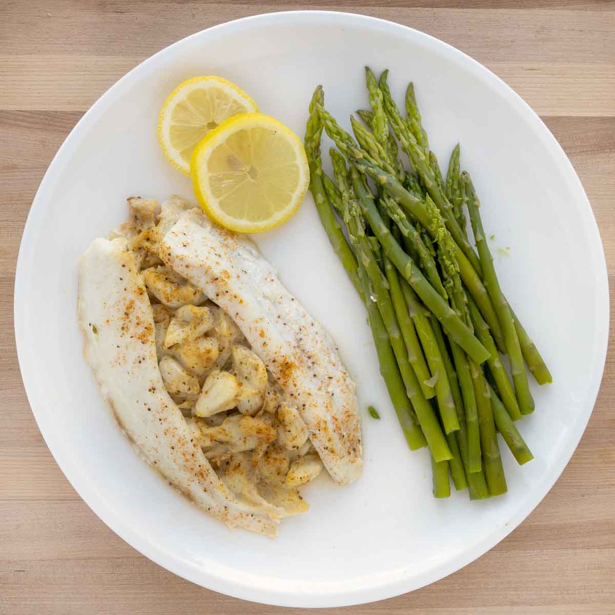overhead view of stuffed flounder and asparagus on a white plate with lemon circles