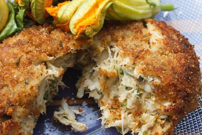lump crab cakes split in half showing the crab filling, garnished with a zucchini blossom