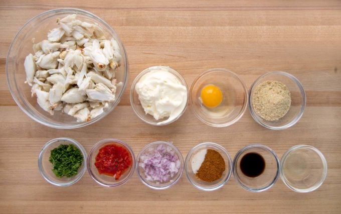 overhead view of ingredients ot make crab cakes in glass bowls on a wooden cutting board