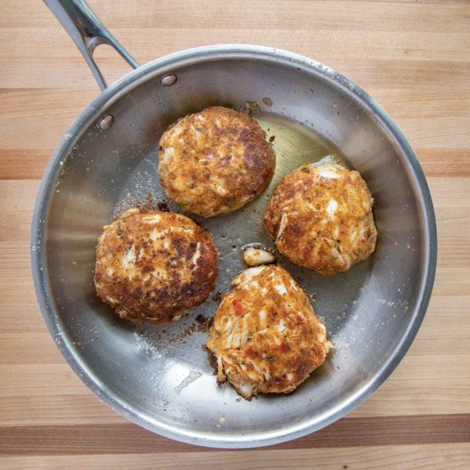 overhead shot of 4 crab cakes in a saute pan on a wooden cutting board