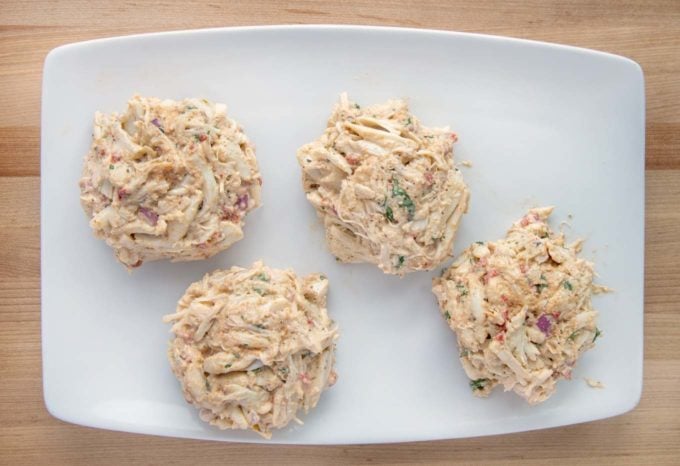 overhead view of 4 unbreaded crab cakes on a white platter