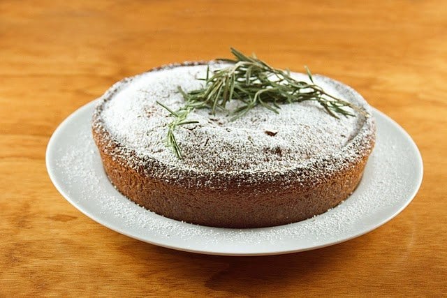 olive oil cake on a white platter with rosemary on top of the cake