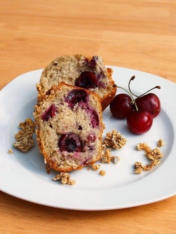 cherry muffin cut in half with 3 cherries on a white plate