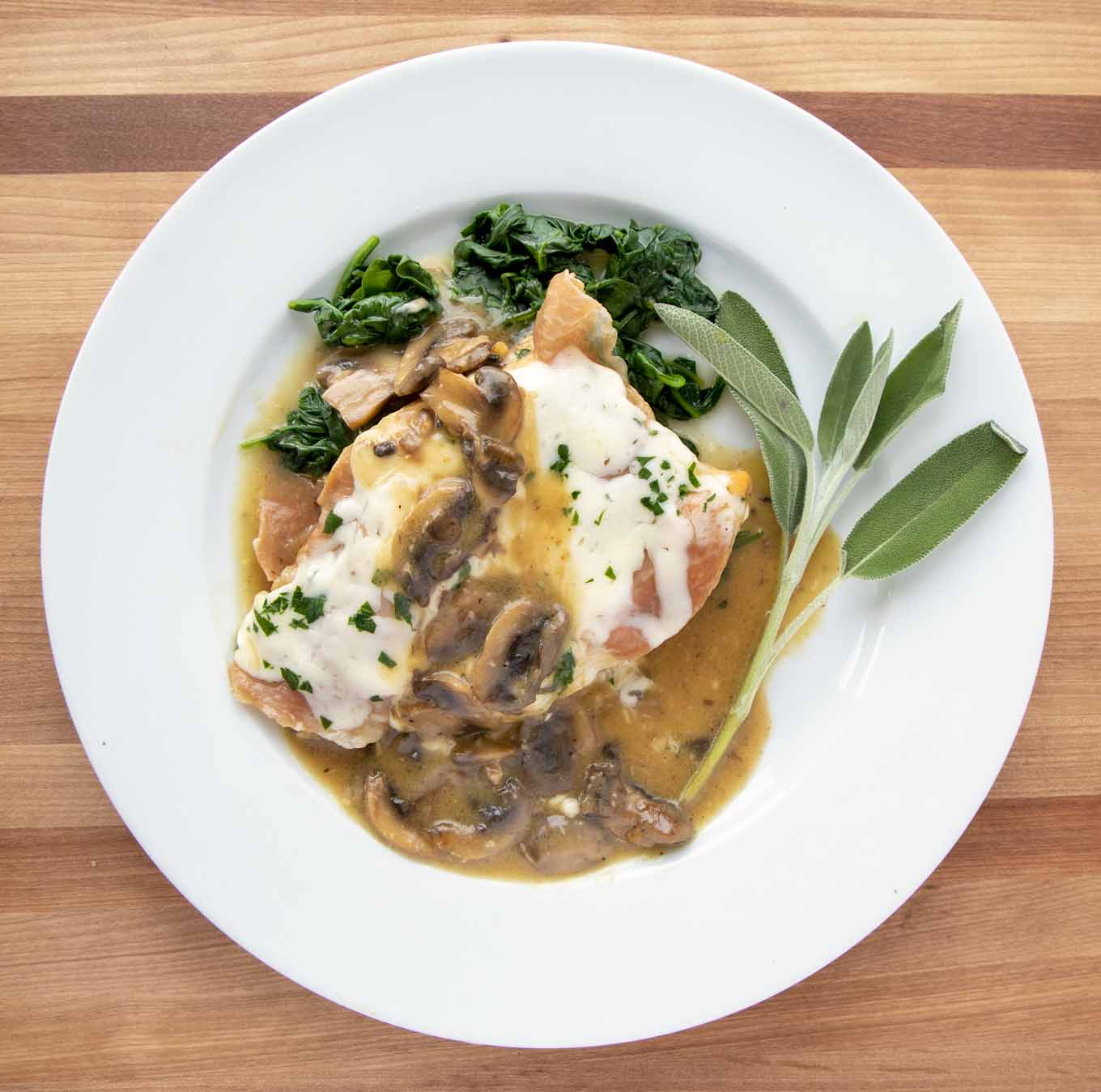 overhead view of chicken saltimbocca on a white plate with a sprig of sage