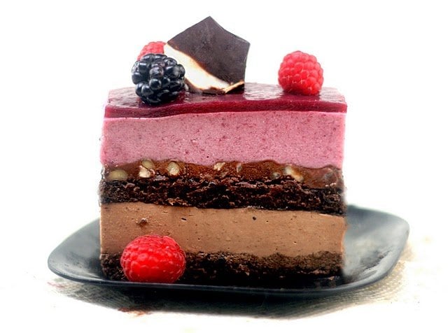 side view of slice of entremet on a black plate with raspberries