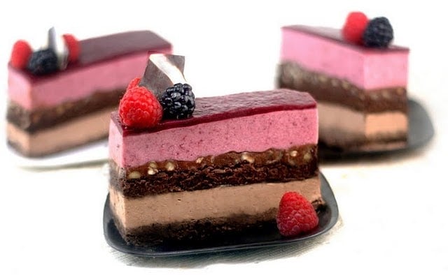 3 slices of entremet on black plates with raspberries