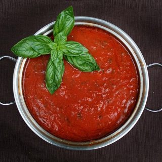 small pot of marinara sauce with a basil garnish sitting on a brown background