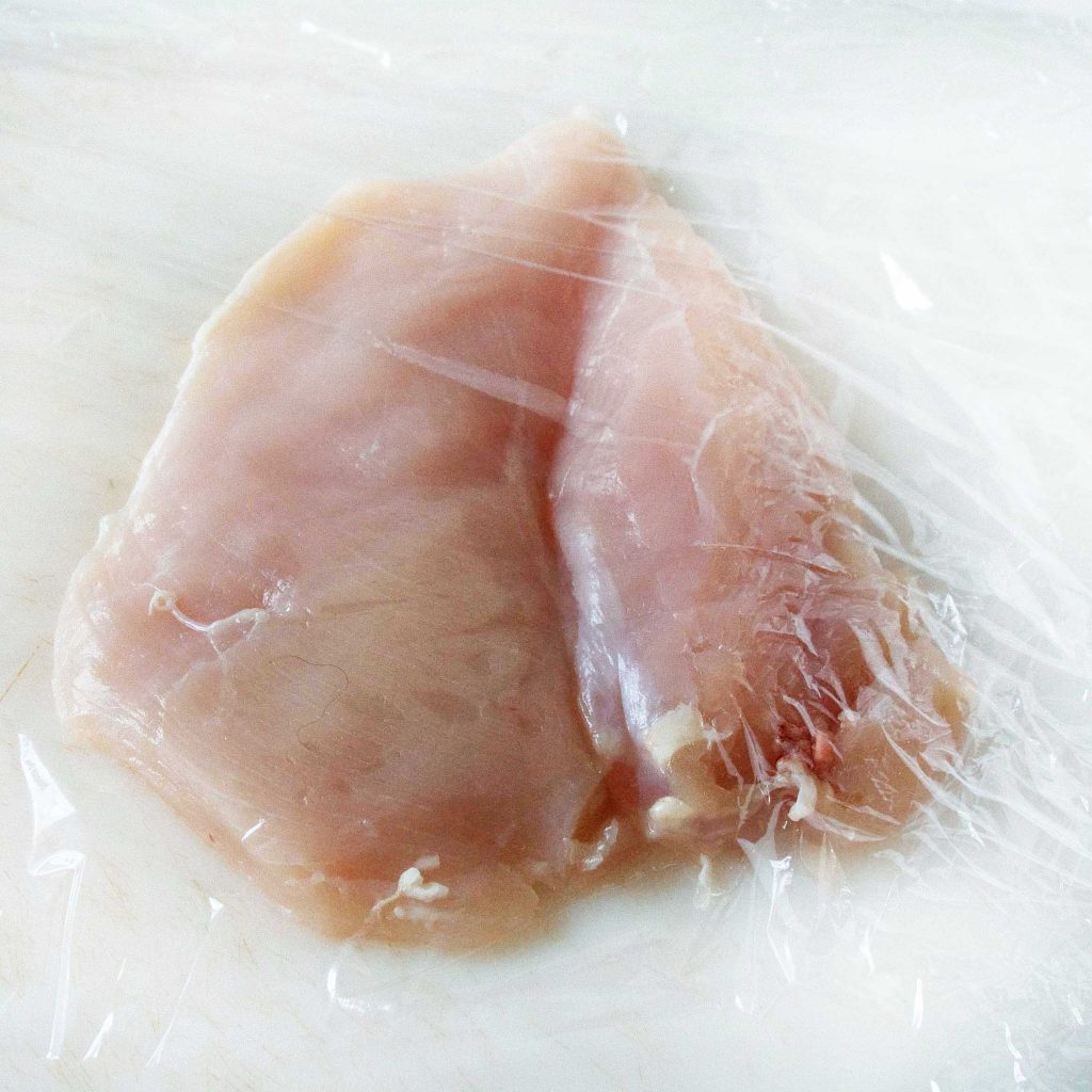 chicken breasts on a cutting board covered with plastic wrap