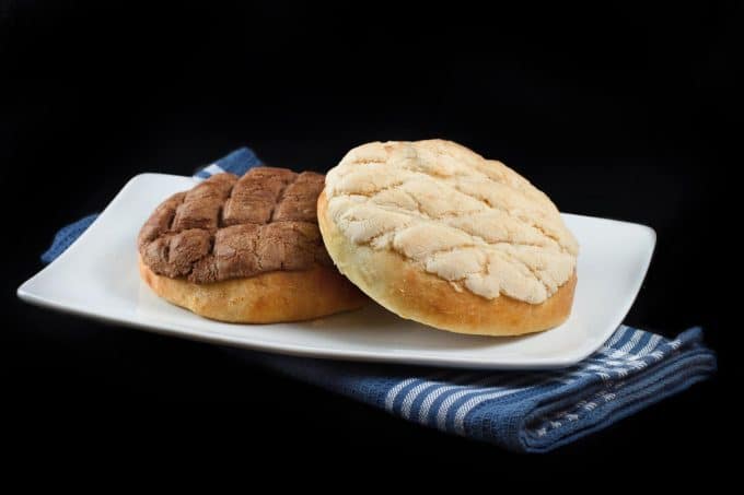 vanilla and chocolate topped pan dulce sitting on a white plate over a blue napkin on a black background