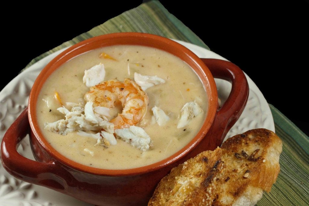 Shrimp and Crab Chowder in a brown crock on a multi colored green napkin on a black background