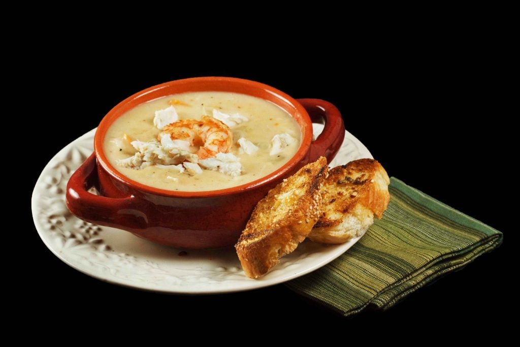 Shrimp and Crab Chowder in a brown crock on a multi colored green napkin on a black background