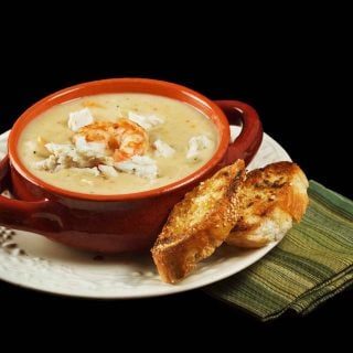 brown crock of shrimp and crab chowder with toasts on a white plate