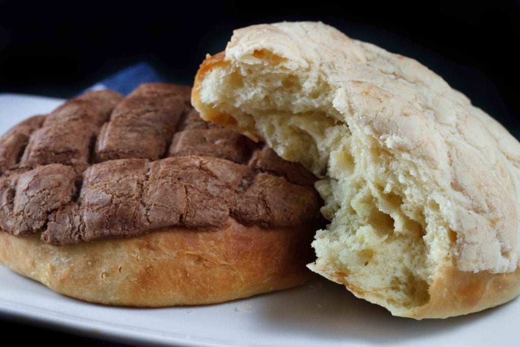 Chocolate Pan dulce with a vanilla pan dulce with a piece torn out so you can see the center sitting on a white plate