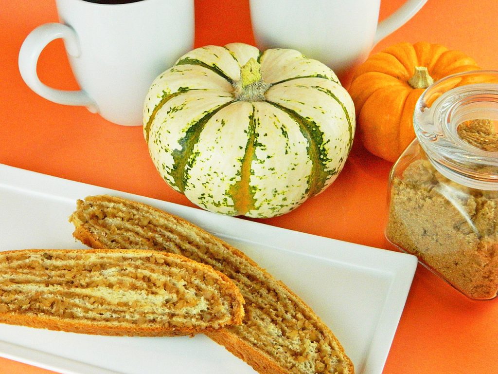 sliced potica on white plate sitting on an orange table with pumpkins and coffee cups in the background