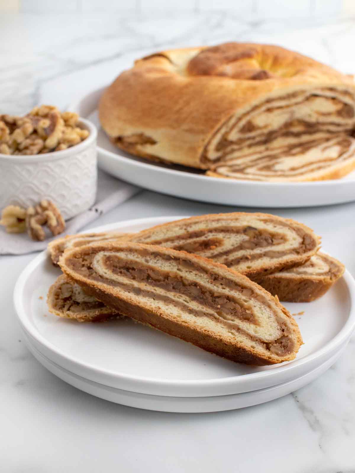 Potica slices of potica on a white plate with remainder of loaf behind it