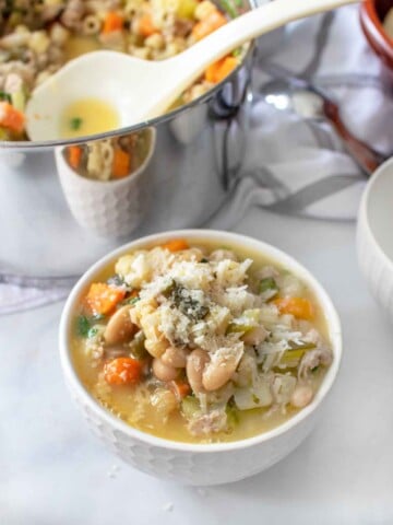 bowl of sausage and bean minestra with the soup pot behind it