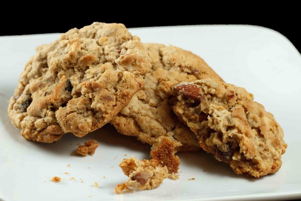  oatmeal granola cookies with a piece missing sitting on a white plate on a black background