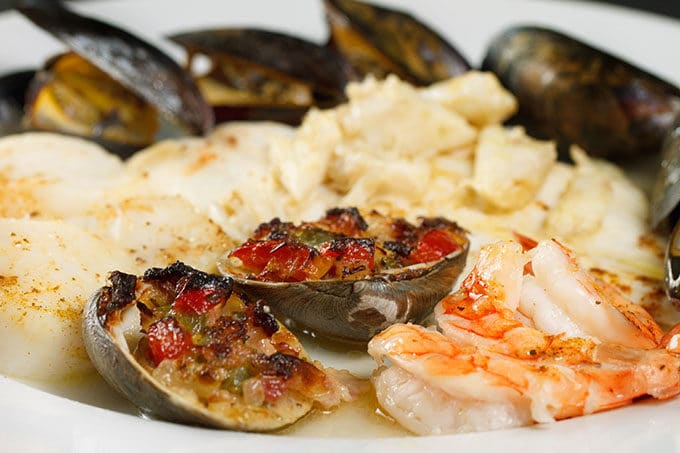 side view of broiled seafood combo on a white plate