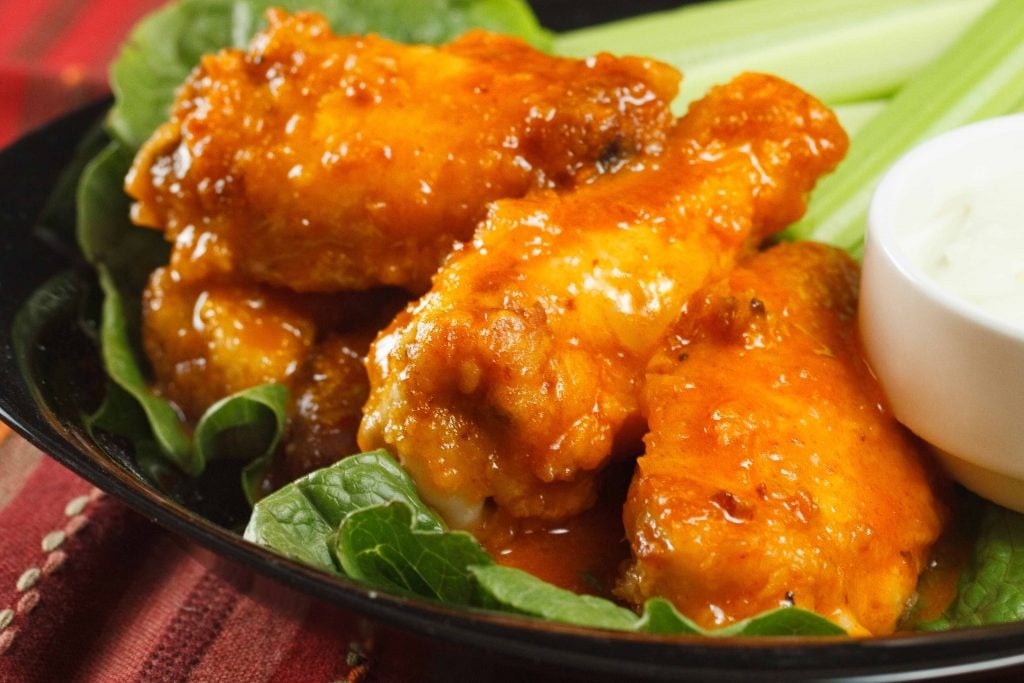 honey lime buffalo wings with blue cheese dressing and celery sticks on a black plate on a multi colored table cloth