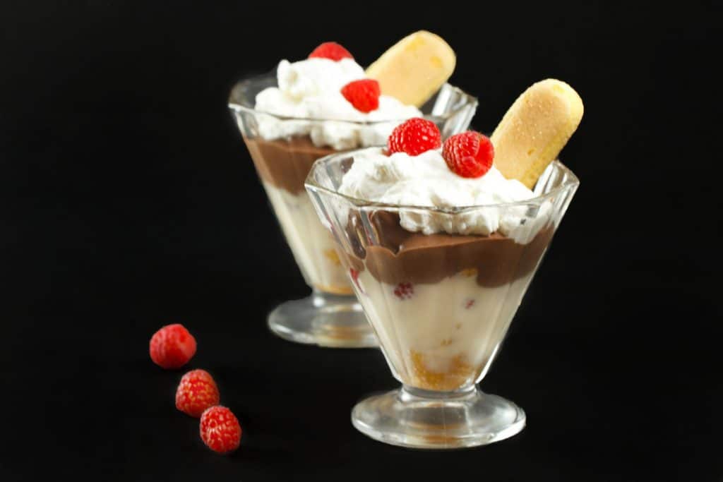 Zuppa Inglese in two clear glass with raspberries and a ladyfinger on top on a black background