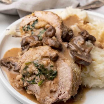 slices of stuffed pork tenderloin on a white plate with mashed potatoes