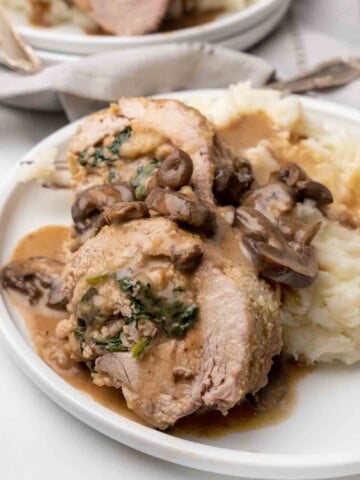 slices of stuffed pork tenderloin on a white plate with mashed potatoes
