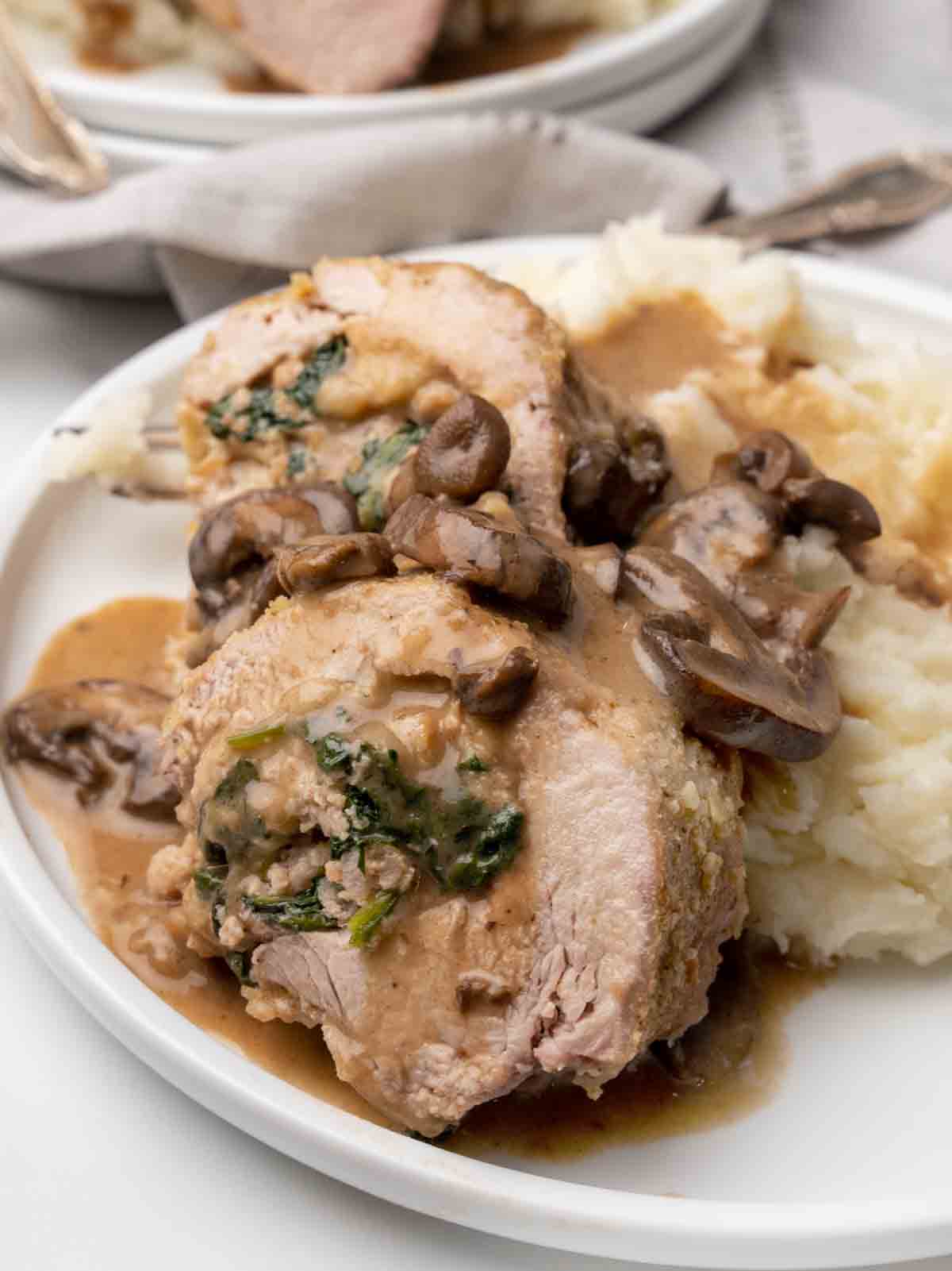 slices of stuffed pork on a white plate with mashed potatoes