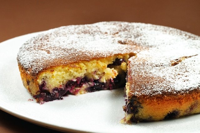 Meyer lemon, blueberry butter cake on a white plate with slice cut out