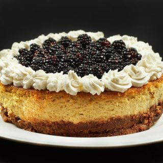 ricotta cheesecake topped with whipped cream and blackberries on a white platter
