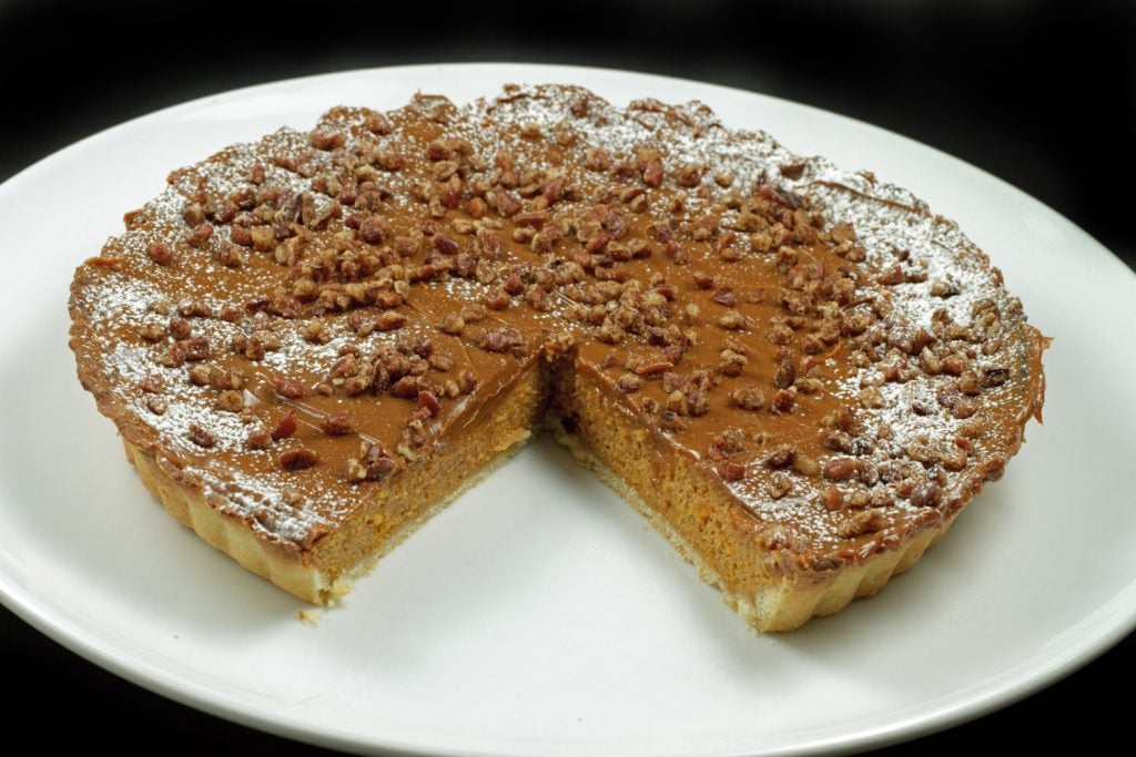 overhead picture of caramel butternut squash torte with cinnamon pecans on a white plate with a slice missing