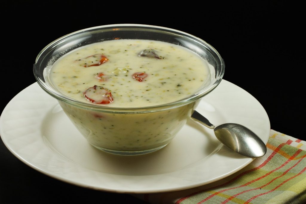 cream of broccoli soup with roasted tomatoes in a glass bowl on a white plate