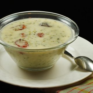 A bowl cream of broccoli soup on a white plate with a spoon