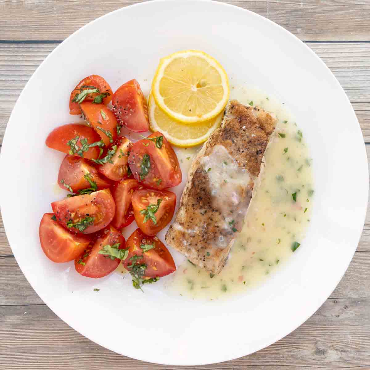 Pan seared tilefish with lemon butter sauce on white plate.