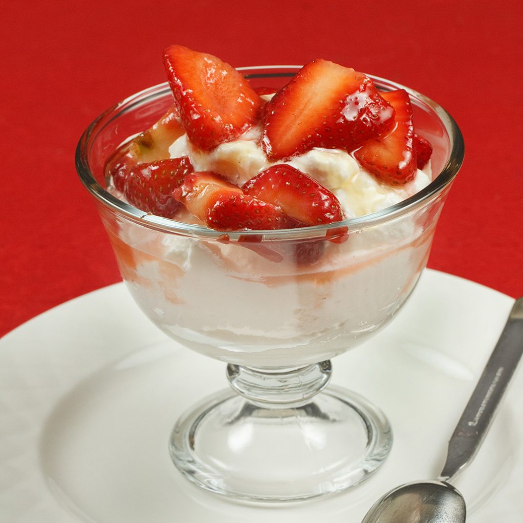 side view of glass dish of honey ricotta mousse with strawberries sitting on a white plate